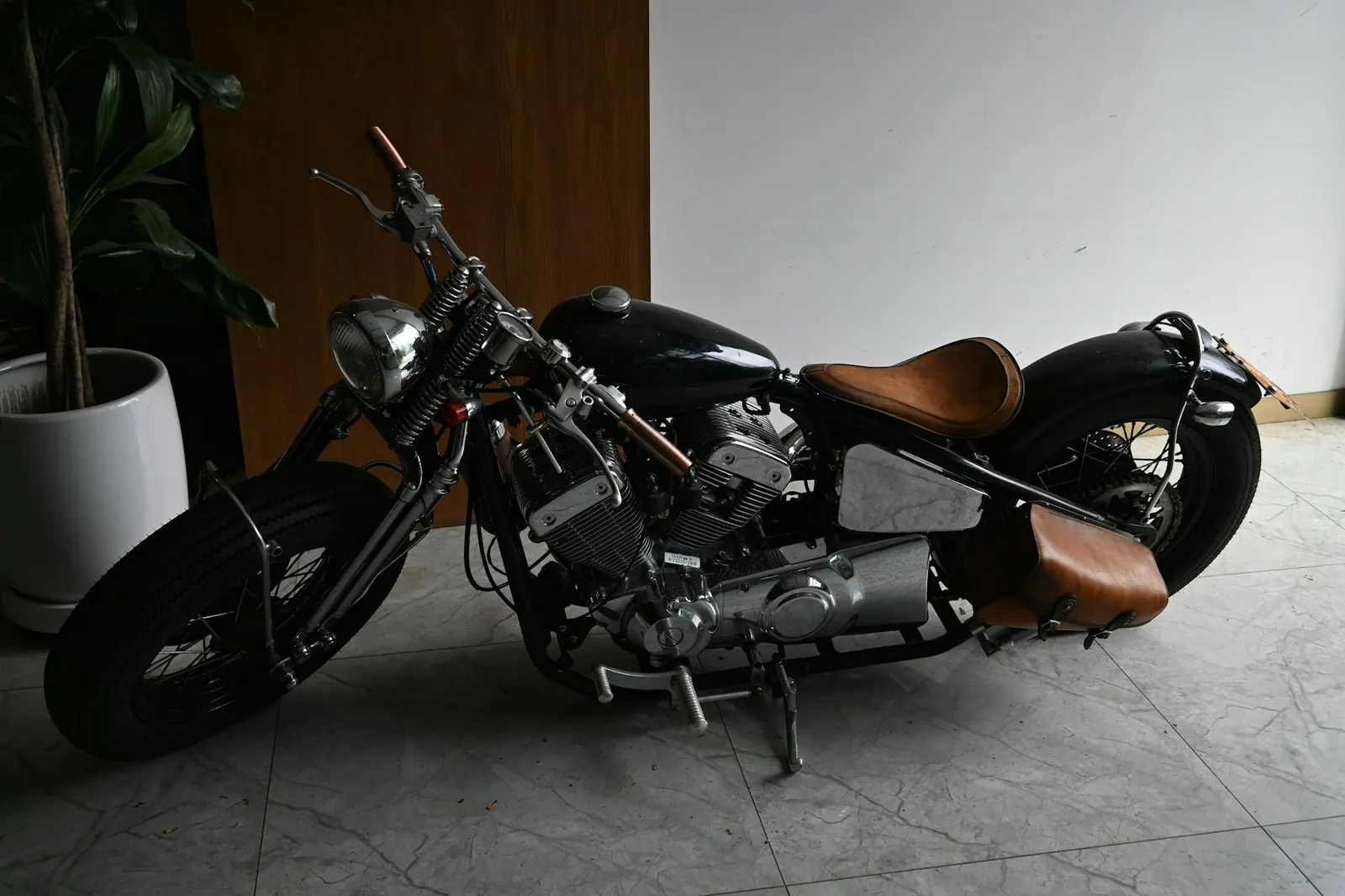 Motor kustom hitam dengan jok cokelat dan tas samping kulit