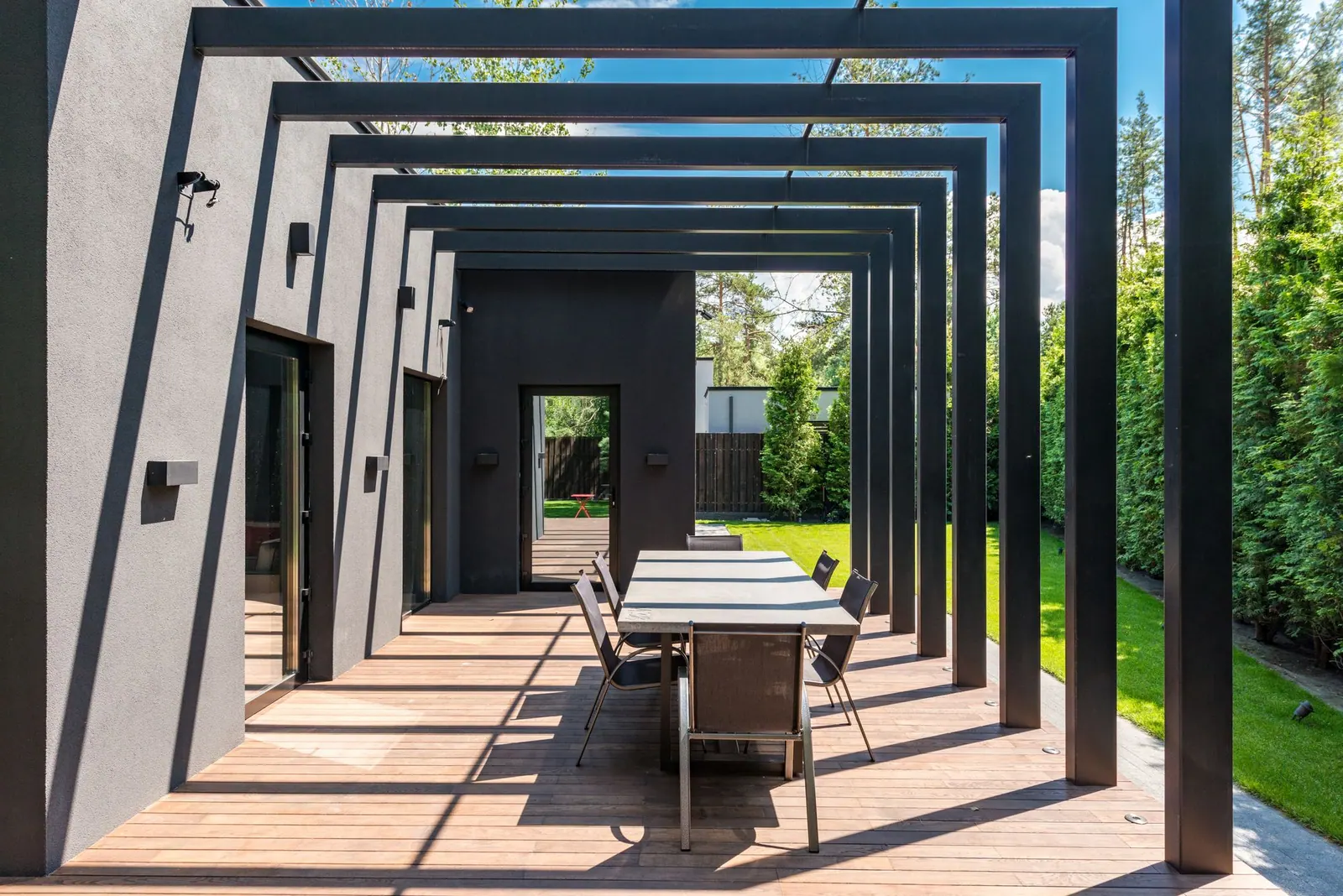 Pergola rangka baja hitam di teras dengan meja makan