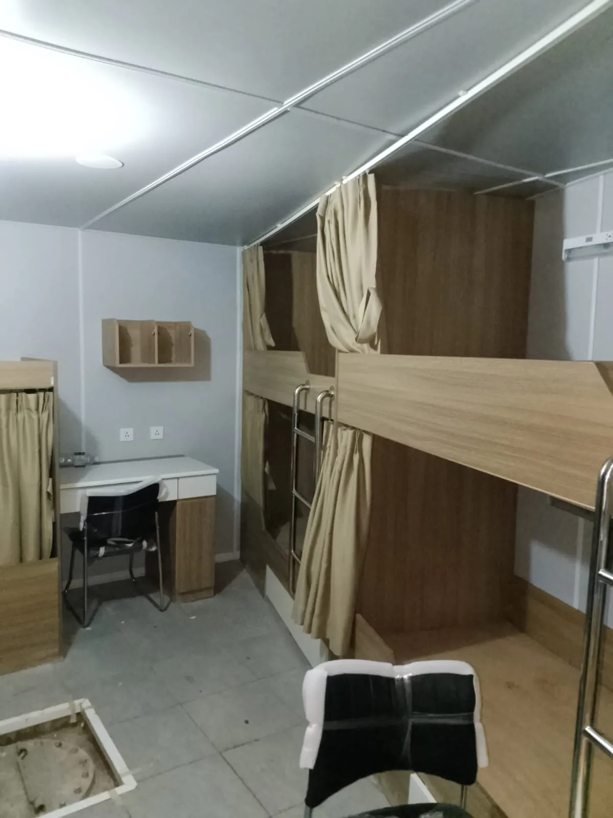 Kabin awak kapal dengan ranjang susun bermotif kayu, gorden krem, meja putih berlaci, dan rak dinding