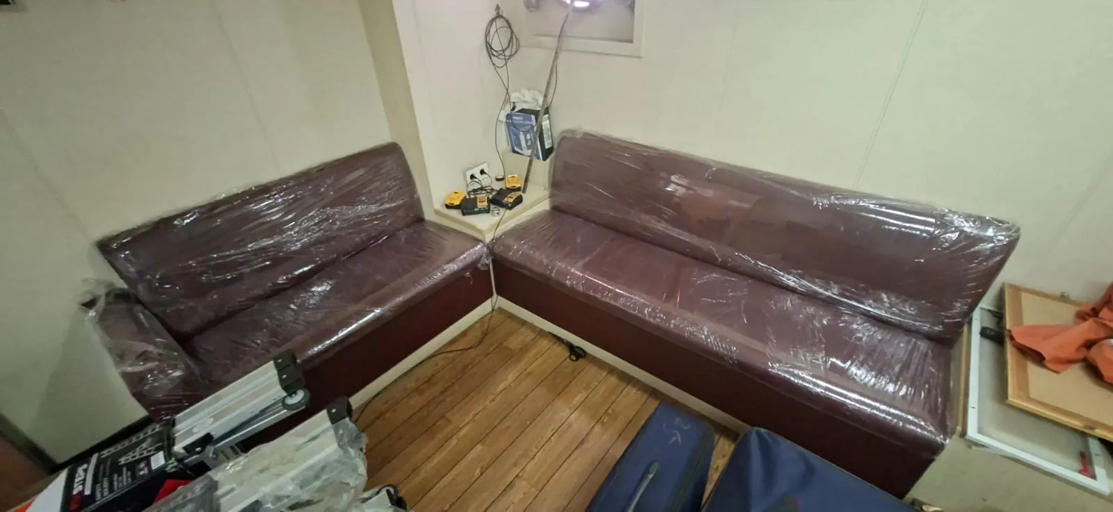 Sofa L berlapis merah marun yang masih terbungkus plastik di ruang duduk kapal berlantai motif kayu